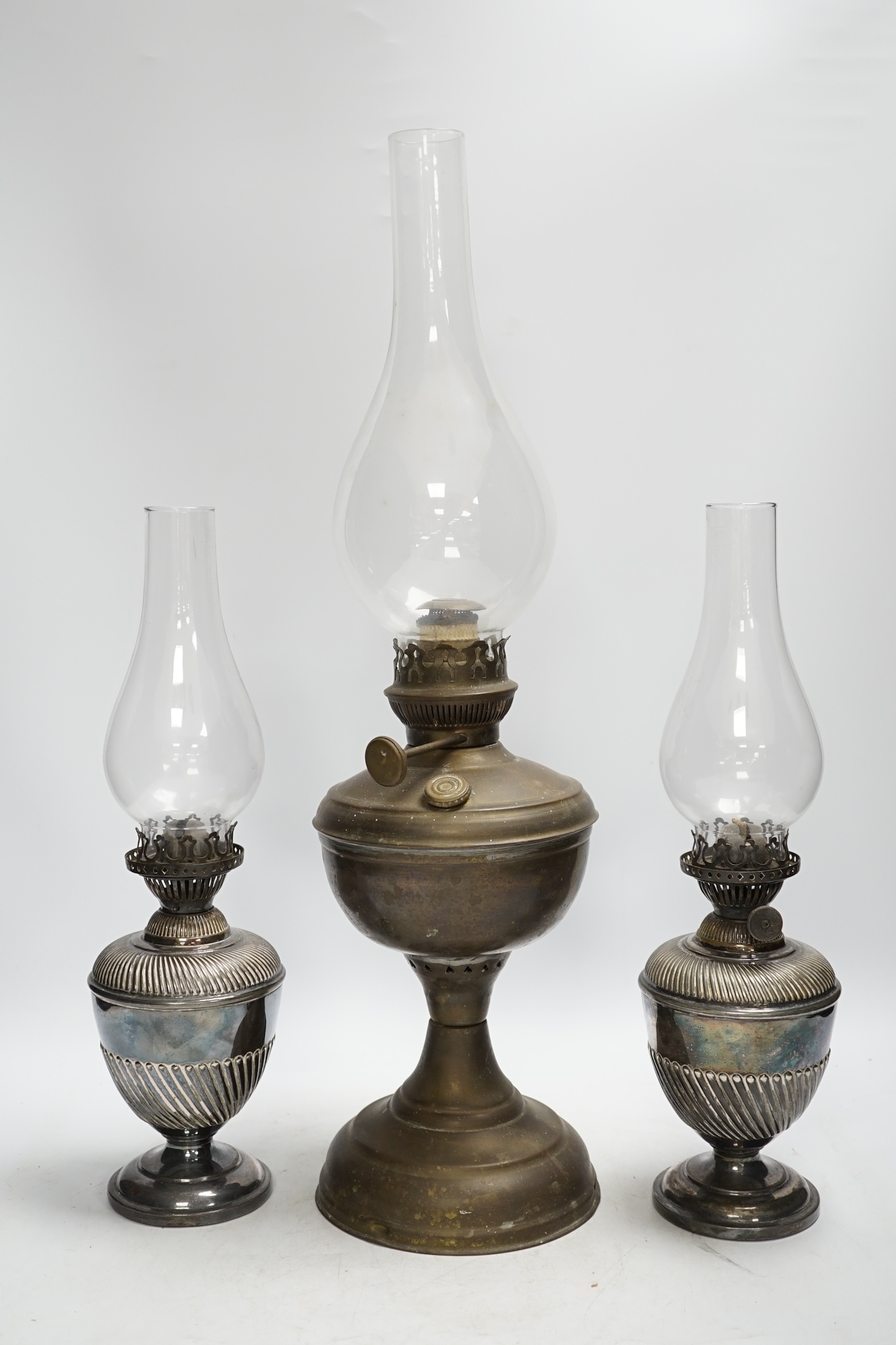 A brass oil lamp and a smaller pair of silver plated oil lamps with glass funnels, tallest including funnel 54cm high. Condition - fair